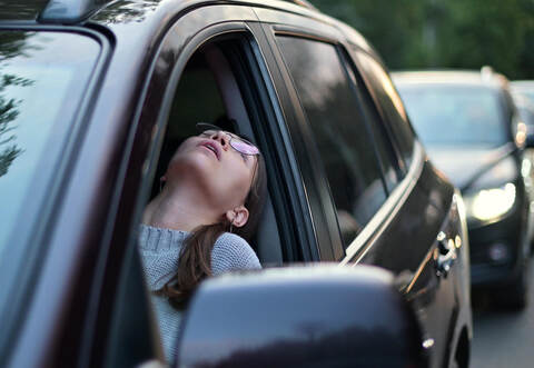 Young woman stands in a traffic jam and looks out through the window
