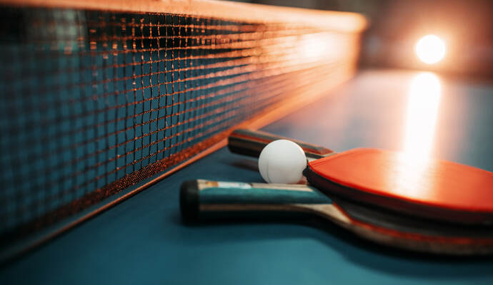 Two tennis rackets and ball against net on table