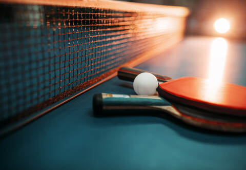 Two tennis rackets and ball against net on table