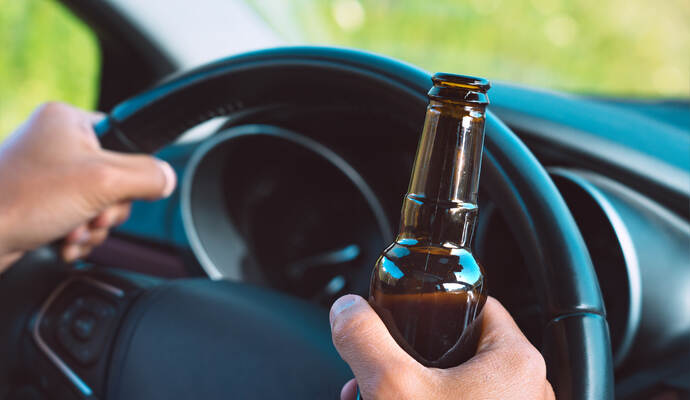 Auf den Fahrer kommt nun eine Anzeige zu. Closeup of drunk driver hands on the steering wheel with a bottle of beer. Driving under alcohol influence