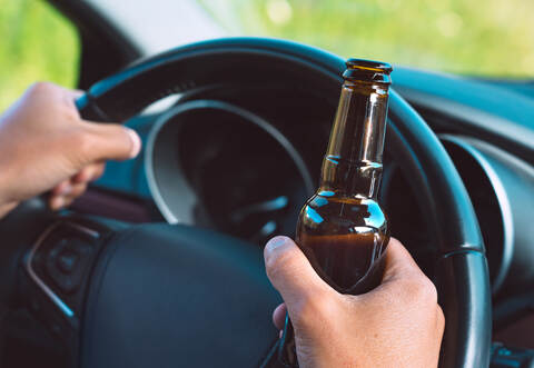 Closeup of drunk driver hands on the steering wheel with a bottle of beer. Driving under alcohol influence