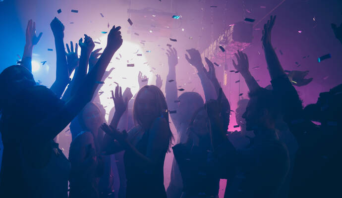 Neu mit von der Partie bei der Schlagerparty ist der Party Kapitän und seine Bläserbande. Close up photo of many party people dancing purple lights confetti flying everywhere nightclub event hands raised up wear shiny