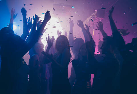Close up photo of many party people dancing purple lights confetti flying everywhere nightclub event hands raised up wear shiny 