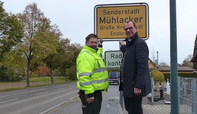OB Frank Schneider (rechts) und Armin Saussele vom Bauhof bei der Einweihung des Schildes an der Ortseinfahrt in der Lomersheimer Straße.