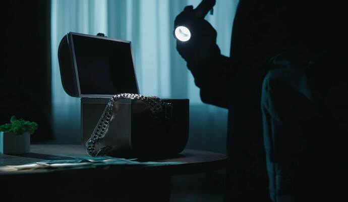 Schmuck in noch unbekannter Höhe haben Diebe in Ispringen erbeutet. A thief commits a burglary, stealing valuables in a dark apartment. A jewelry box illuminated by a beam from a lantern in the ha