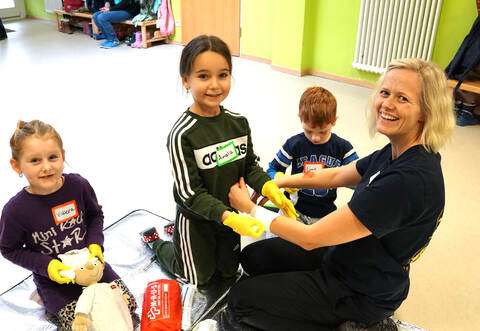 Lehrkraft Tanja Mesitschek zeigt den Kindern spielerisch an einer Puppe, wie man Verletzten hilft.