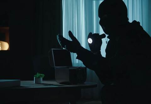 A thief in a black balaclava commits a burglary, stealing valuables. Criminal in a dark apartment with a flashlight close up. Cr