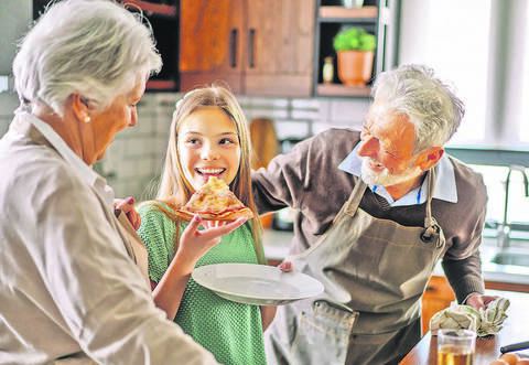 Happy family with grandparent and child in kitchen eating pizza