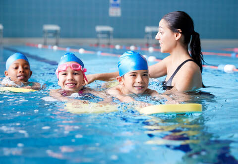Female Coach In Water Giving Group Of Children Swimming Lesson In Indoor Pool
