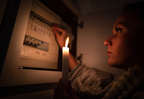 Woman checking fuse box at home during power outage or blackout. No electricity concept