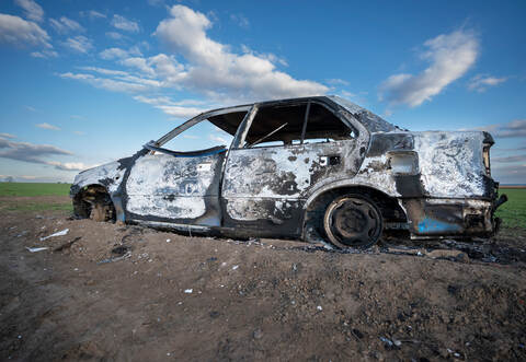 A burned out car. Burnt car in the field. Car fire, vehicle fire due to short circuit. Stolen car intentional arson. One vehicle